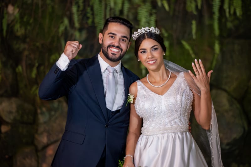 Noivos comemorando, ele de punho erguido e ela mostrando a aliança