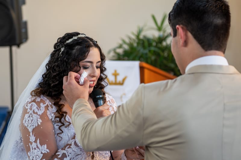 Noivo enxugando as lágrimas da noiva durante os votos