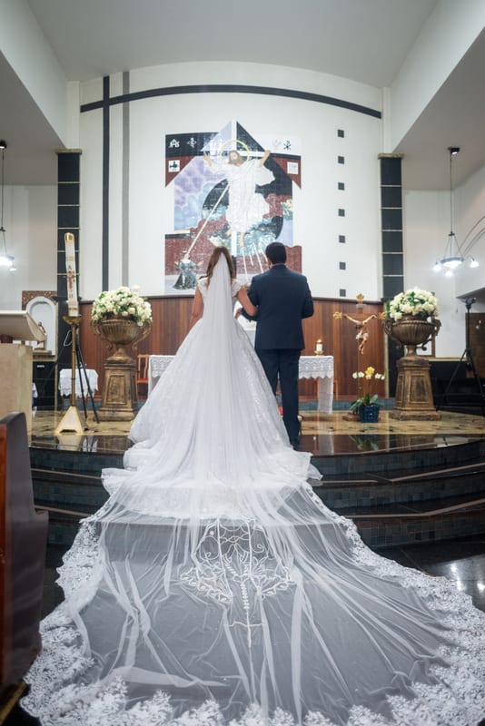 Noivos de costas diante do altar, com o véu longo espalhado pelo chão