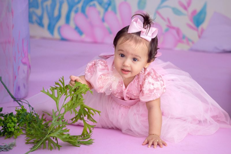Bebê de laço rosa engatinhando num cenário florido